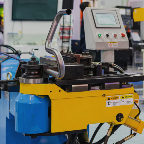 CSM metal tube bending machine with touchscreen in a steel stockholder factory showing the mandrel machine pushing out a piece of bent tube to be used as a chair leg in the manufacturing process.